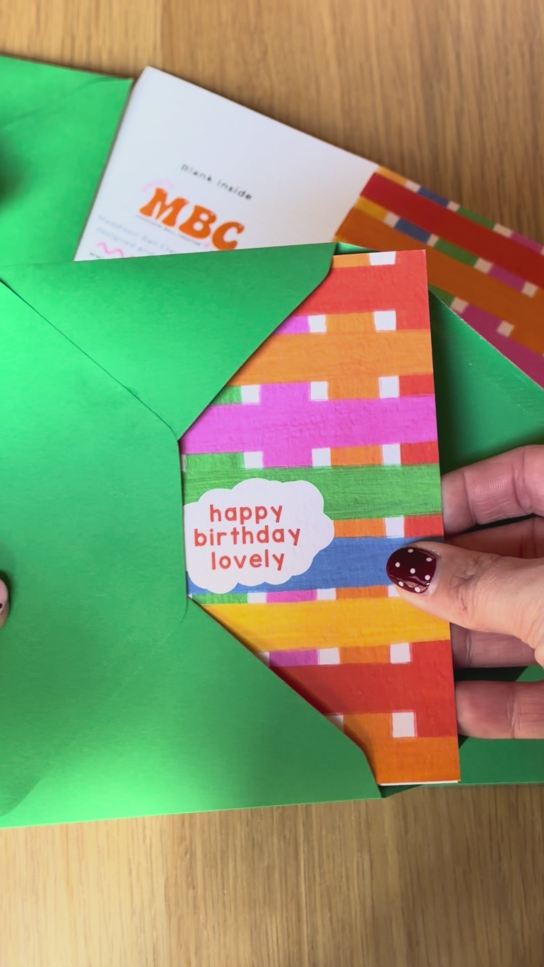 Colourful greeting card with striped pattern and 'happy birthday lovely' text getting pulled out of green envelope
